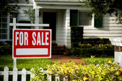 A for sale sign is in front of a white house.