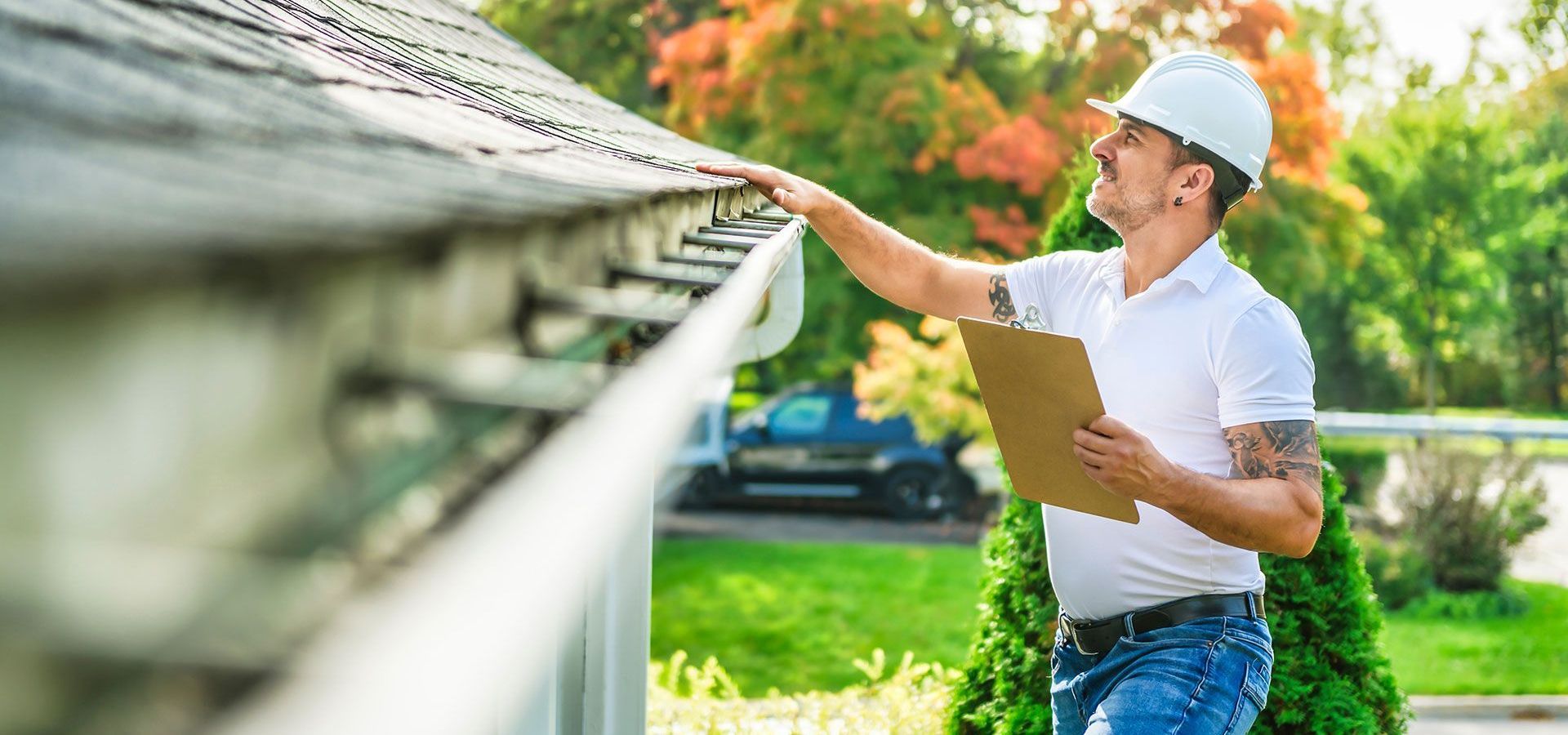A man is looking at a gutter on a roof while holding a clipboard.