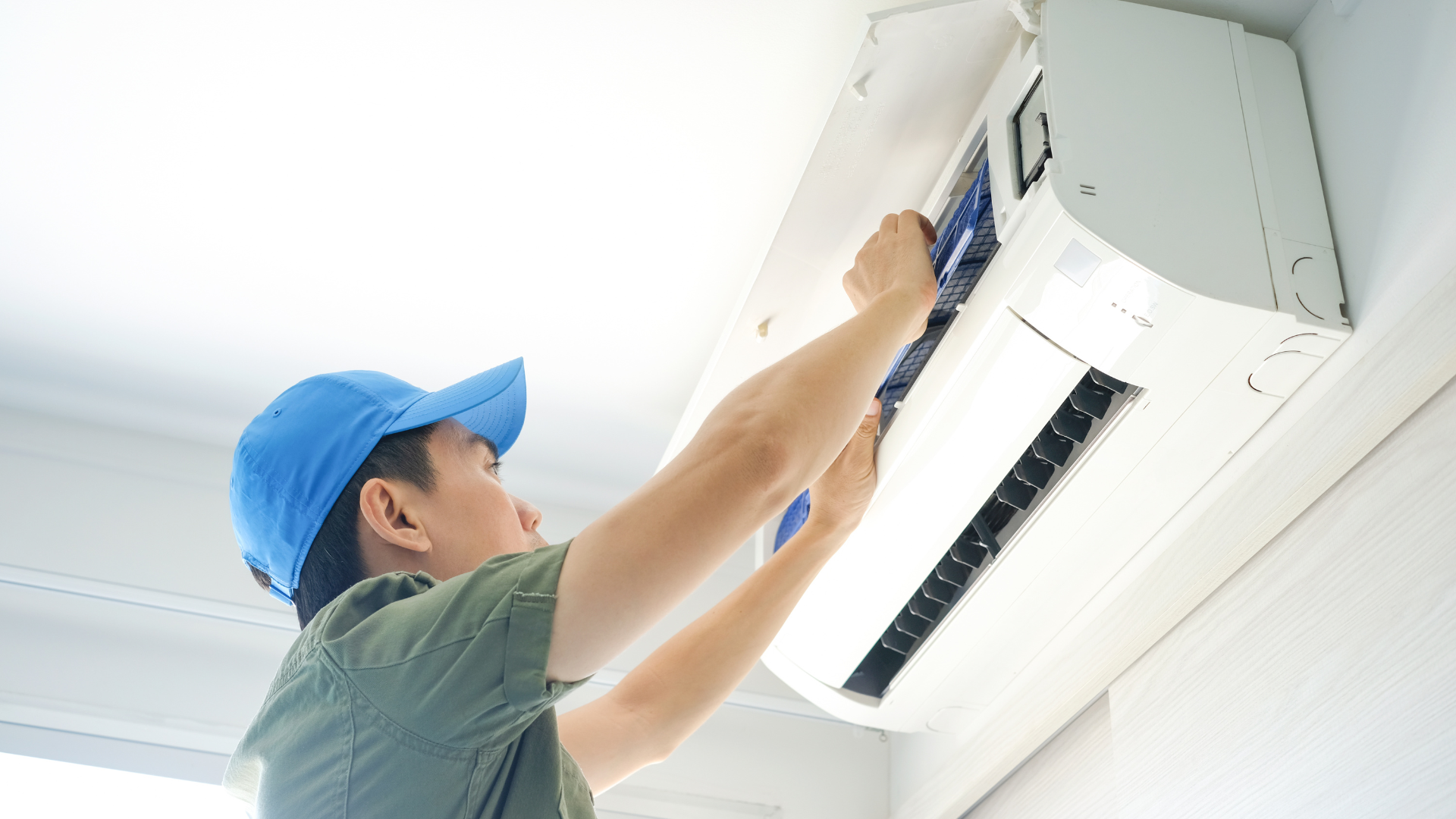 A man in a blue hat is fixing an air conditioner.