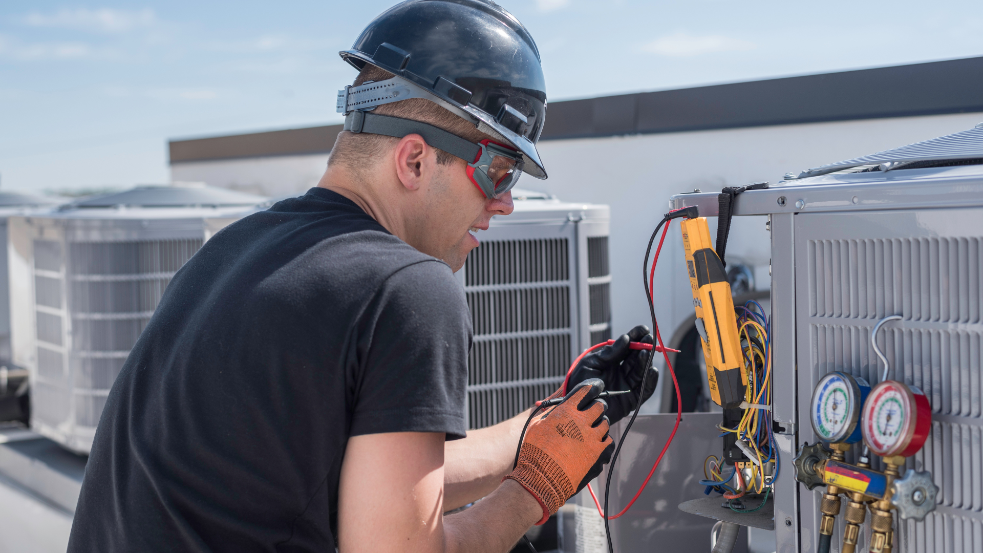 A man is working on an air conditioner on top of a building.