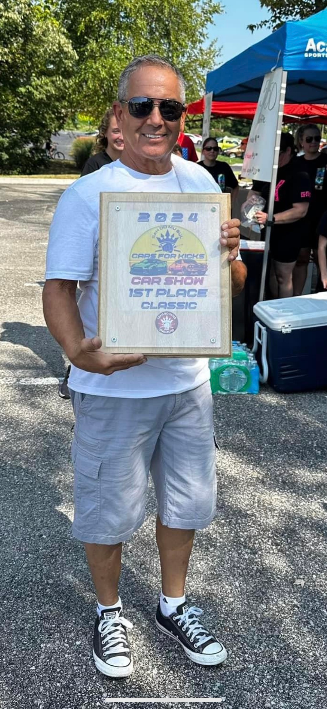 A man is standing in a parking lot holding a framed certificate.
