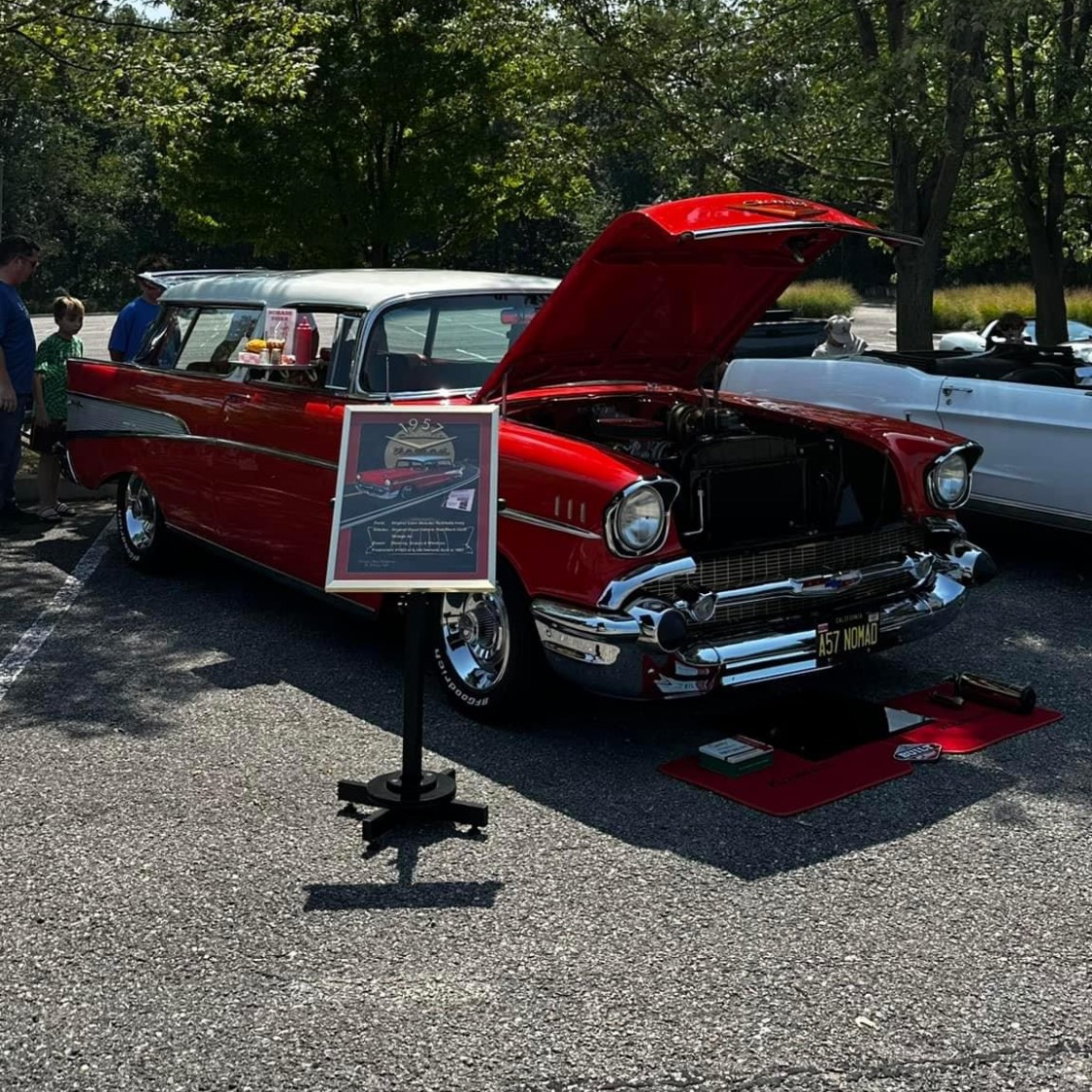 A red car with the hood up is on display at a car show.