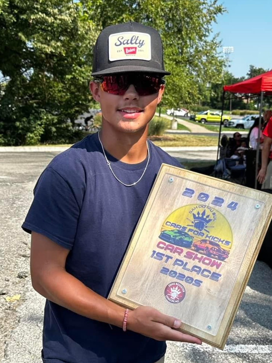 A young man wearing a hat and sunglasses is holding a plaque.