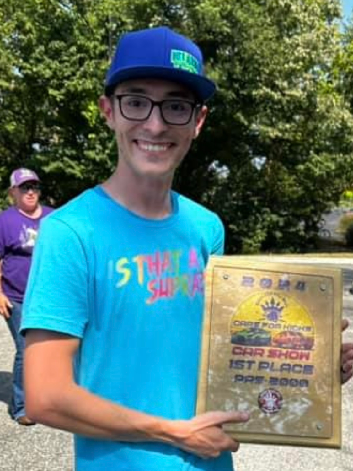 A young man wearing a blue hat and glasses is holding a plaque.