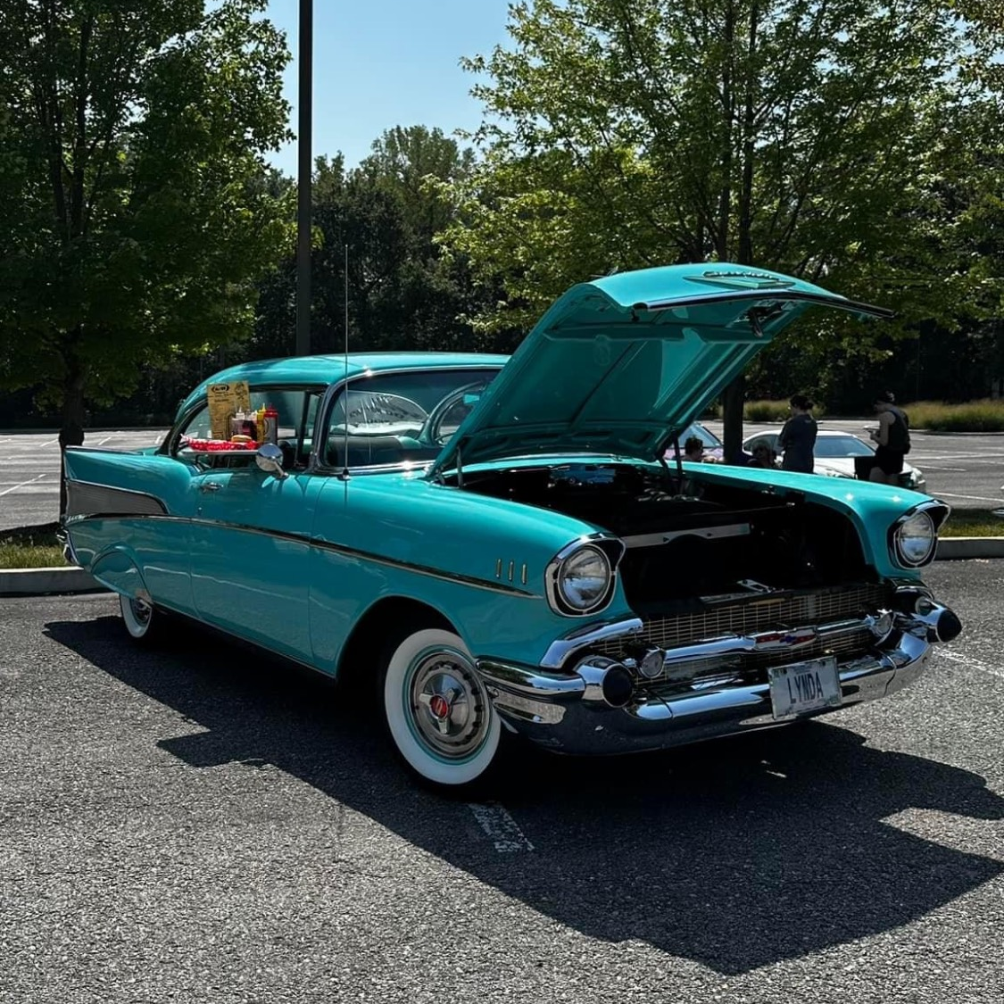A blue car with the hood up is parked in a parking lot