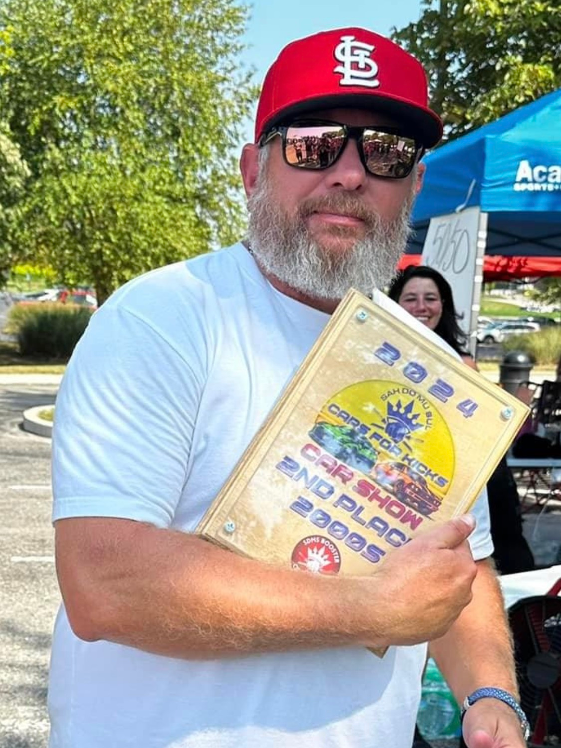 A man wearing a red hat and sunglasses is holding a certificate.