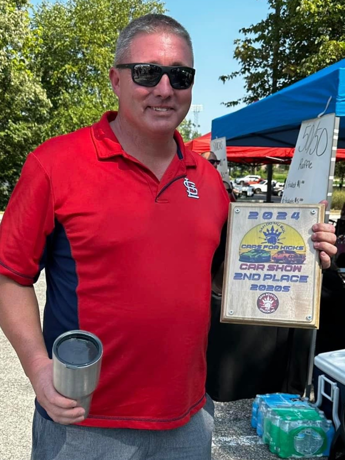 A man in a red shirt is holding a cup and a certificate.