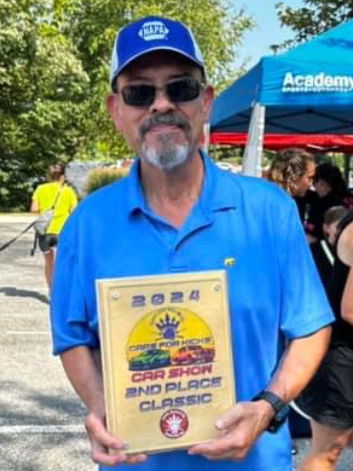 A man in a blue shirt is holding a car show 2nd place classic award