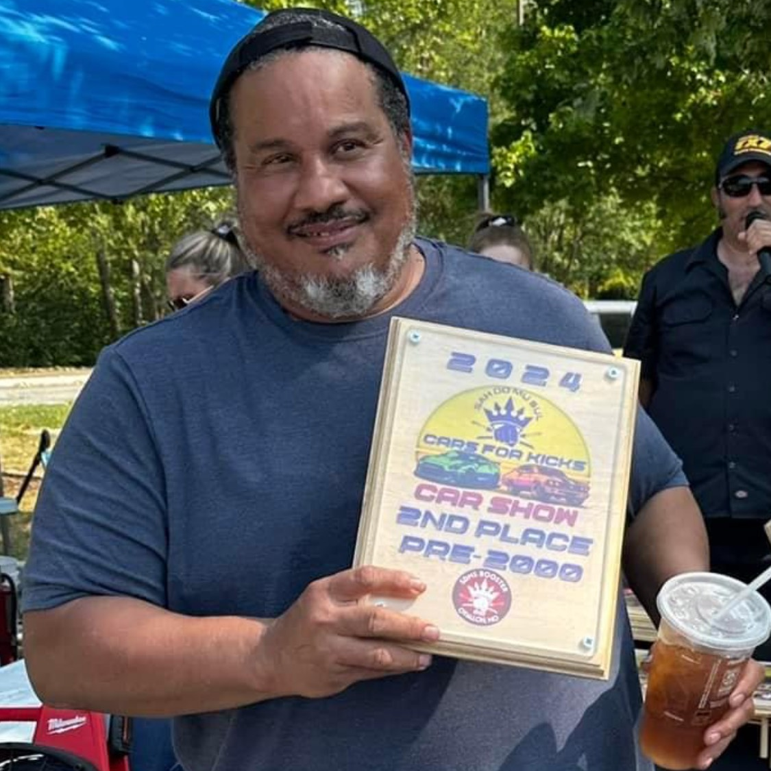 A man is holding a plaque that says car show 2nd place pre 2000