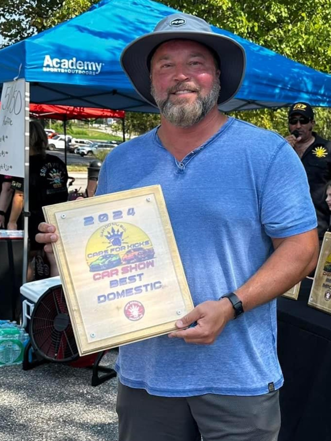 A man in a hat is holding a framed certificate that says best domestic car show.