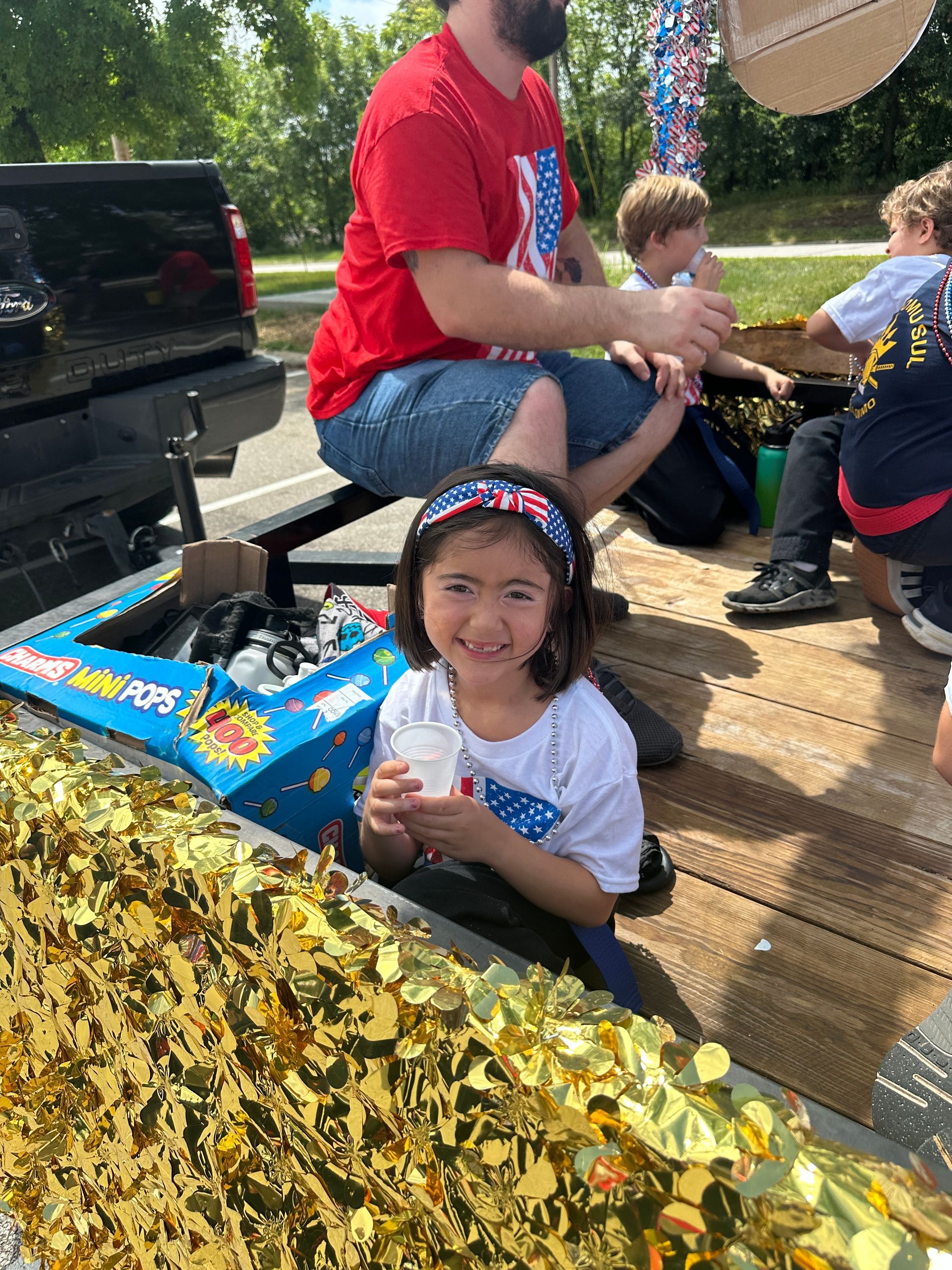 A little girl is sitting in the back of a truck with a man.