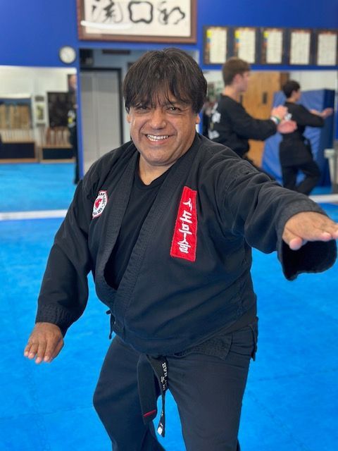 A man in a black karate uniform is standing on a blue mat.