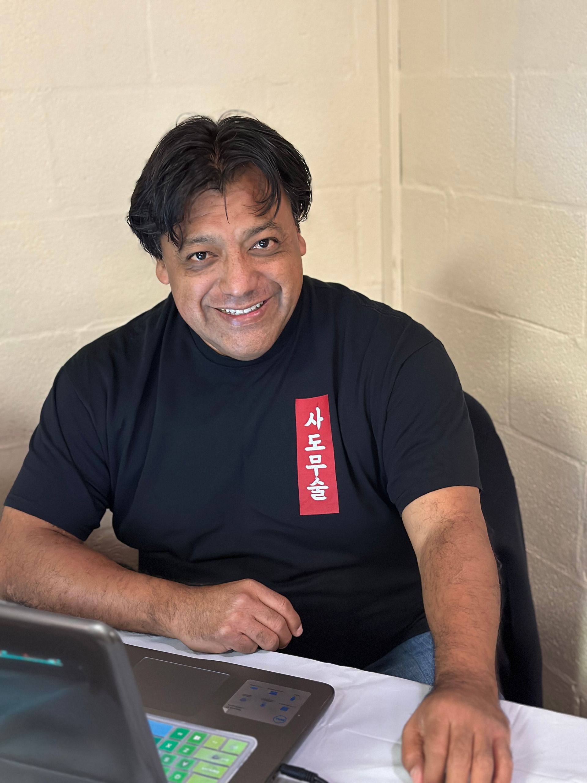 A man in a black shirt is sitting at a table with a laptop.