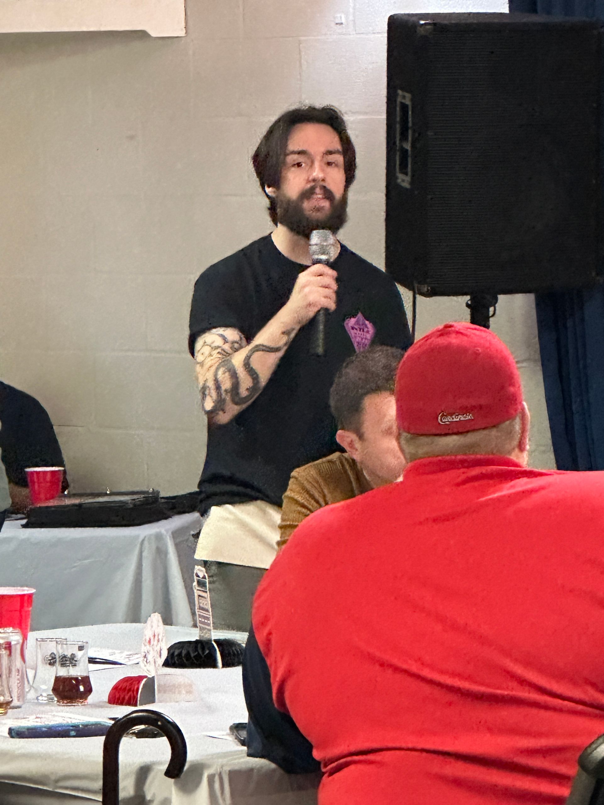 A man with a beard is holding a microphone in front of a group of people.