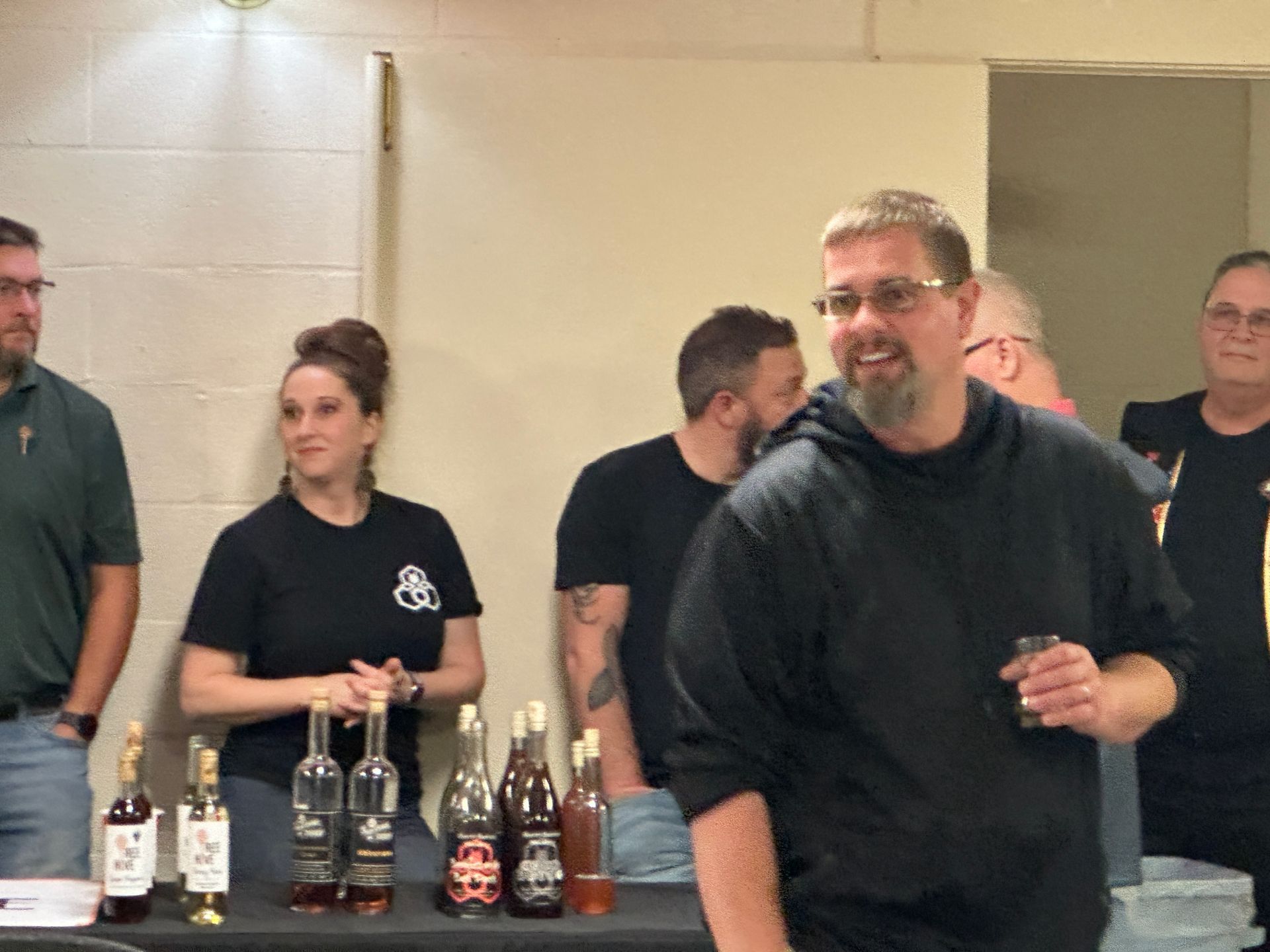 A group of people are standing around a table with bottles of alcohol on it.
