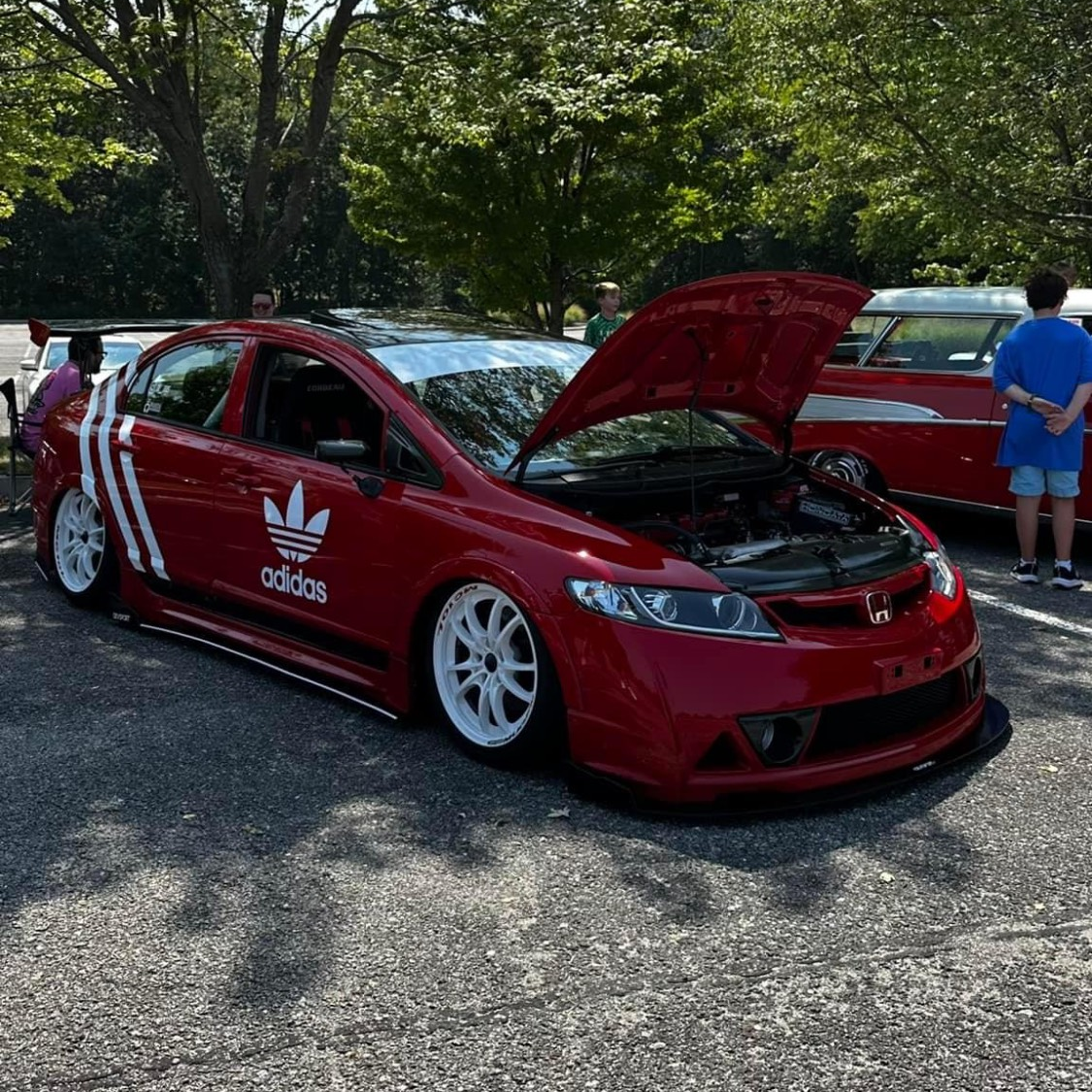 A red car with the hood up is parked in a parking lot.