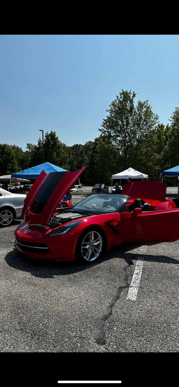 A red sports car with the hood up is parked in a parking lot.