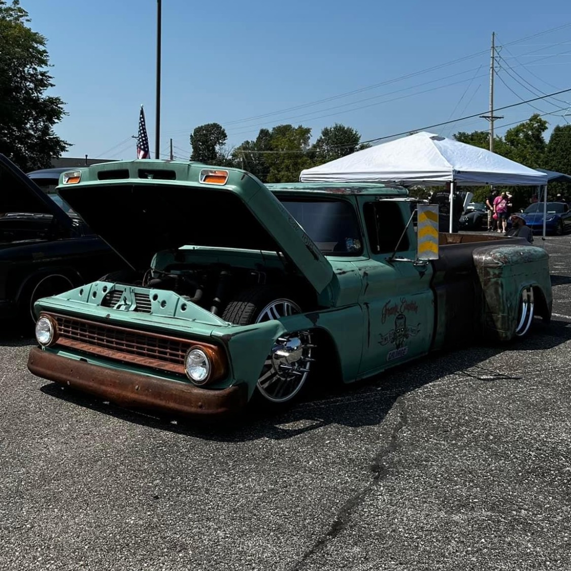 A green truck with the hood up is parked in a parking lot