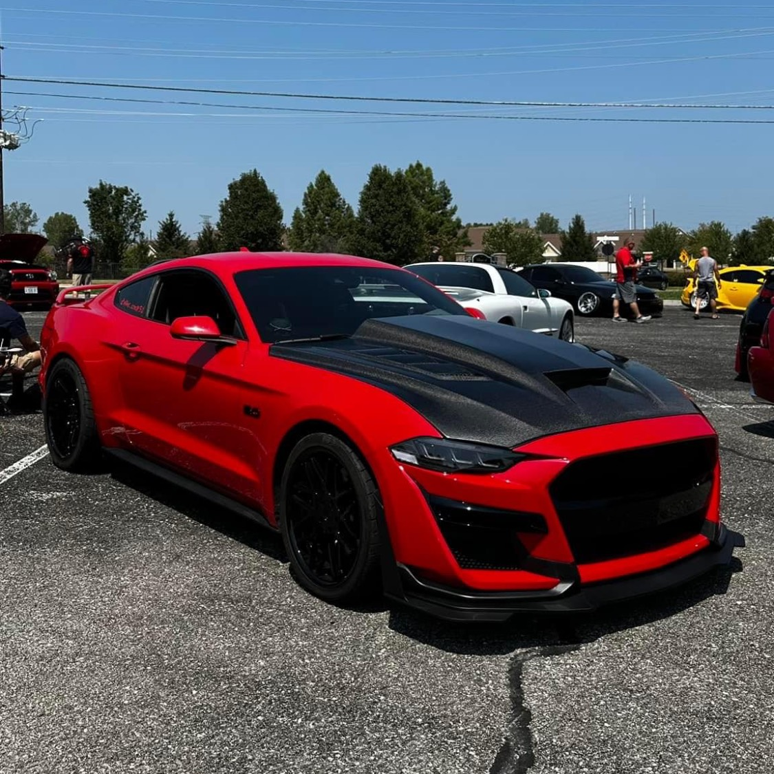 A red car with a black hood is parked in a parking lot