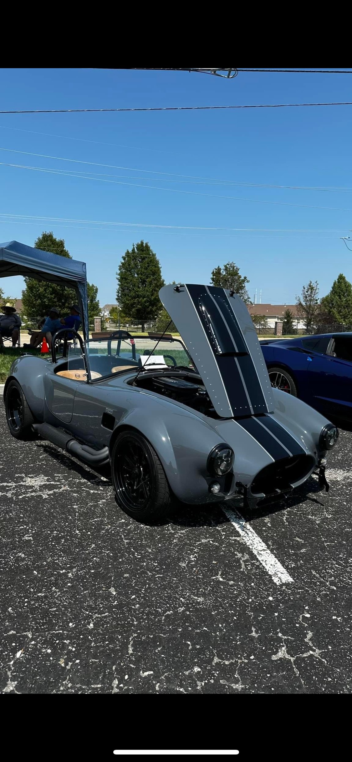 A gray sports car with the hood up is parked in a parking lot.