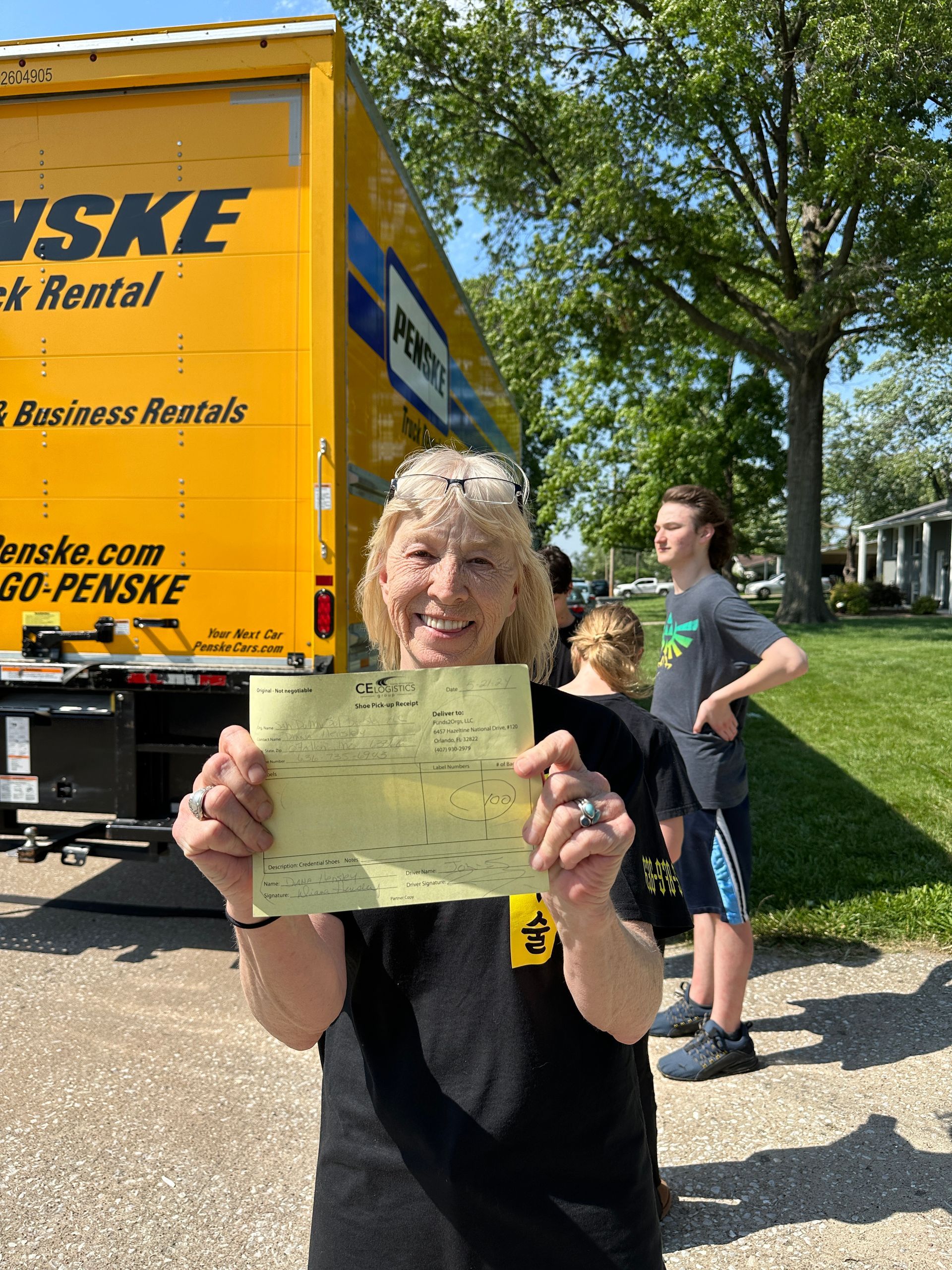 A woman is holding a check in front of a moving truck.