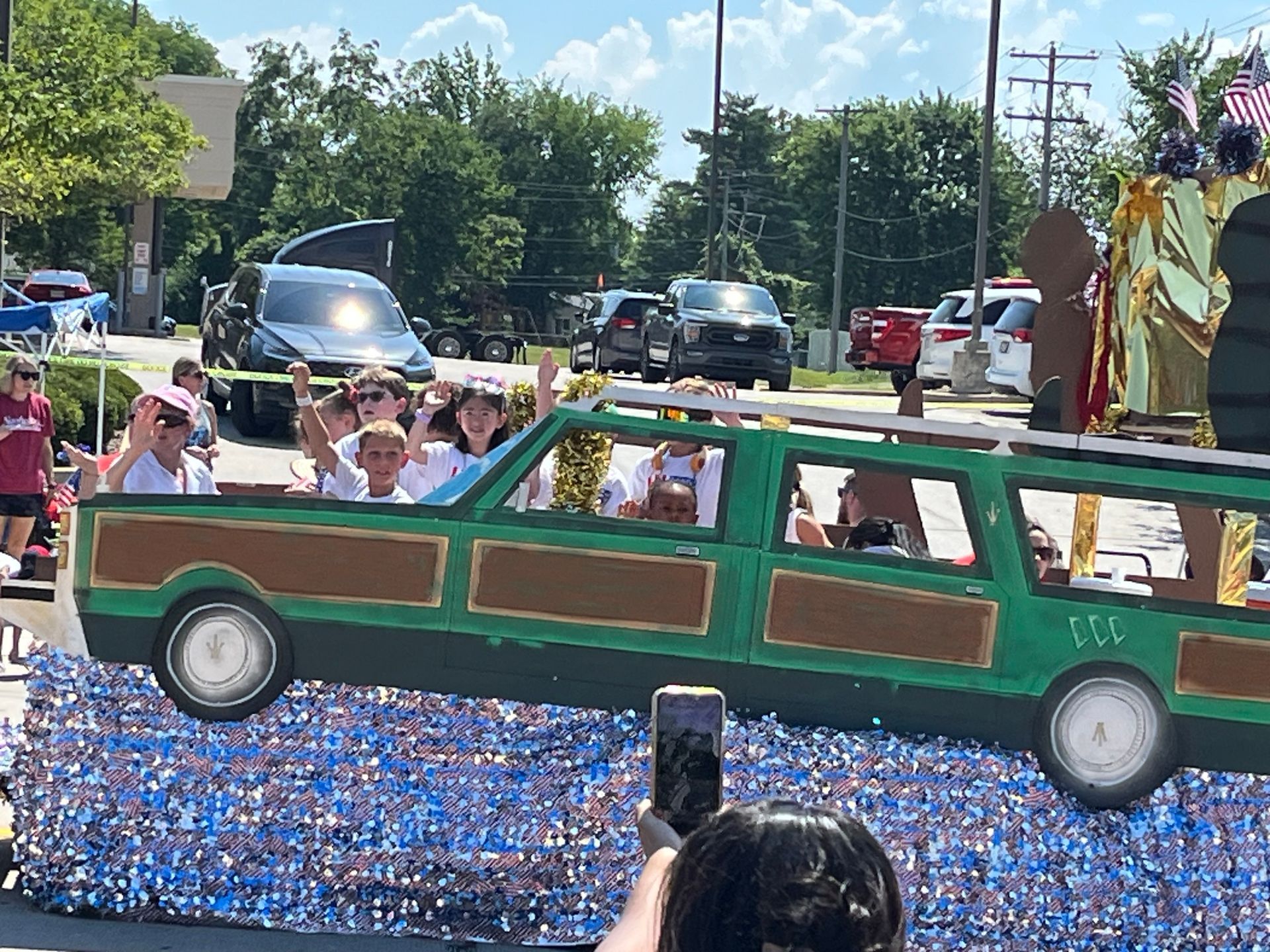 A group of people are riding in a parade float designed to look like the Grizwald's station wagon.