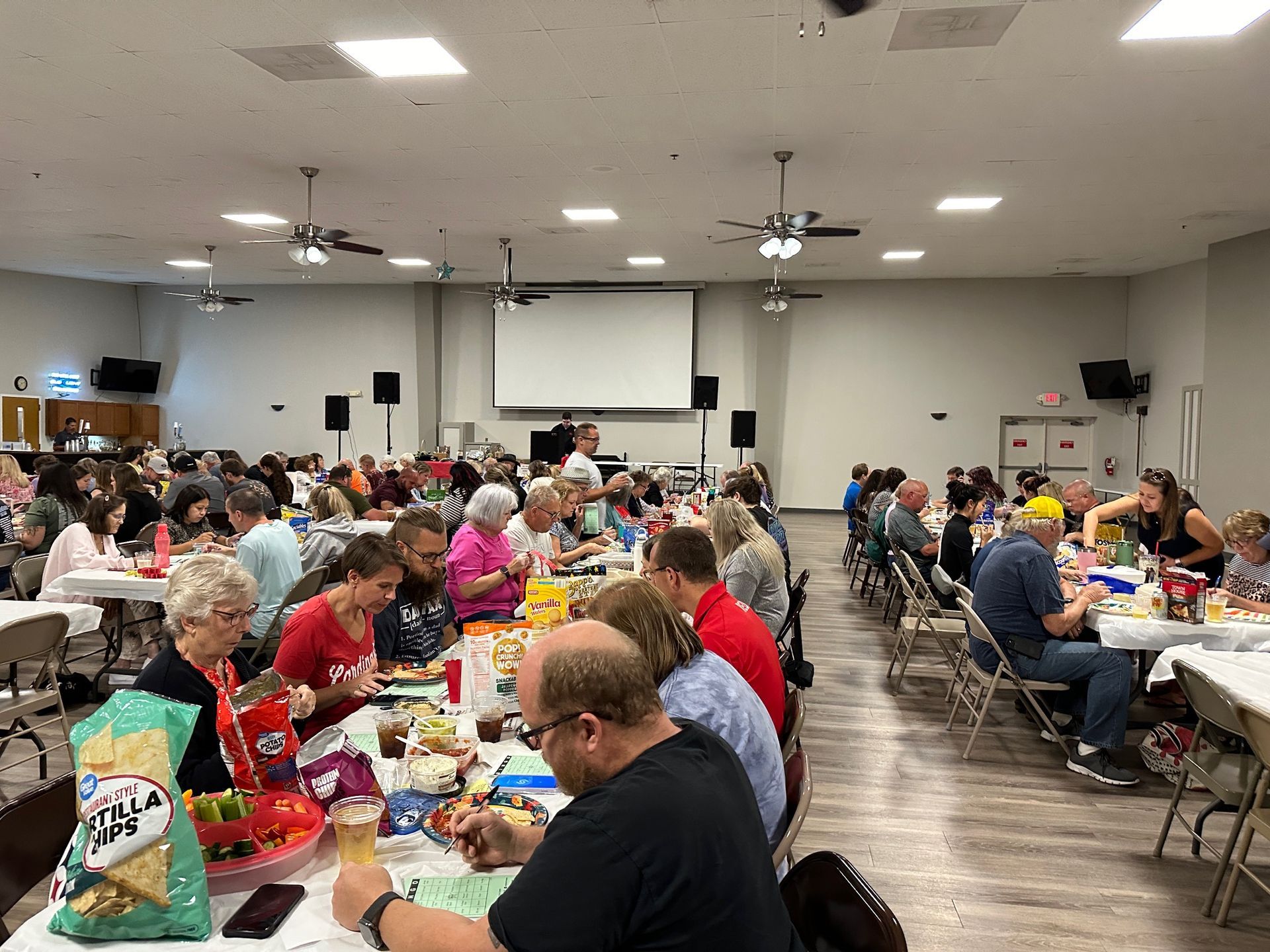 A large group of people are sitting at tables in a large room eating food.