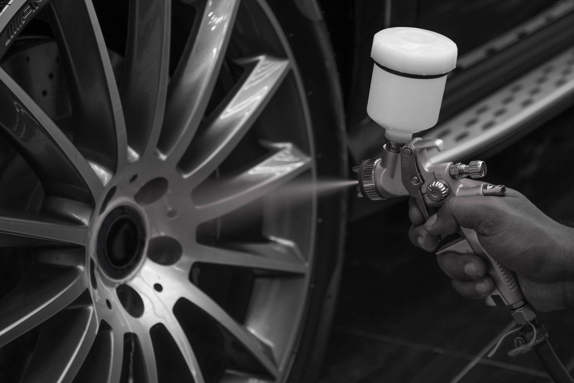 Spray gun painting a silver car wheel rim in a workshop