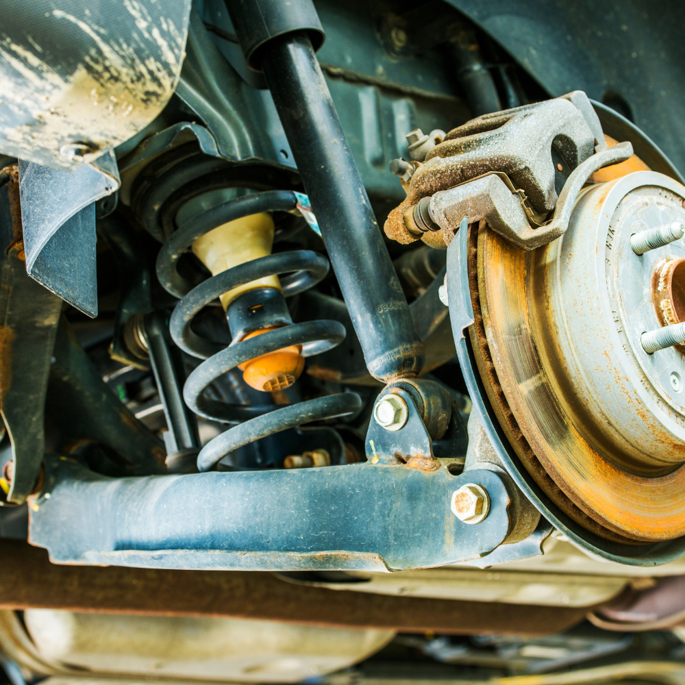 Close-up of a vehicle suspension with spring, shock absorber, and brake assembly on a dusty undercarriage