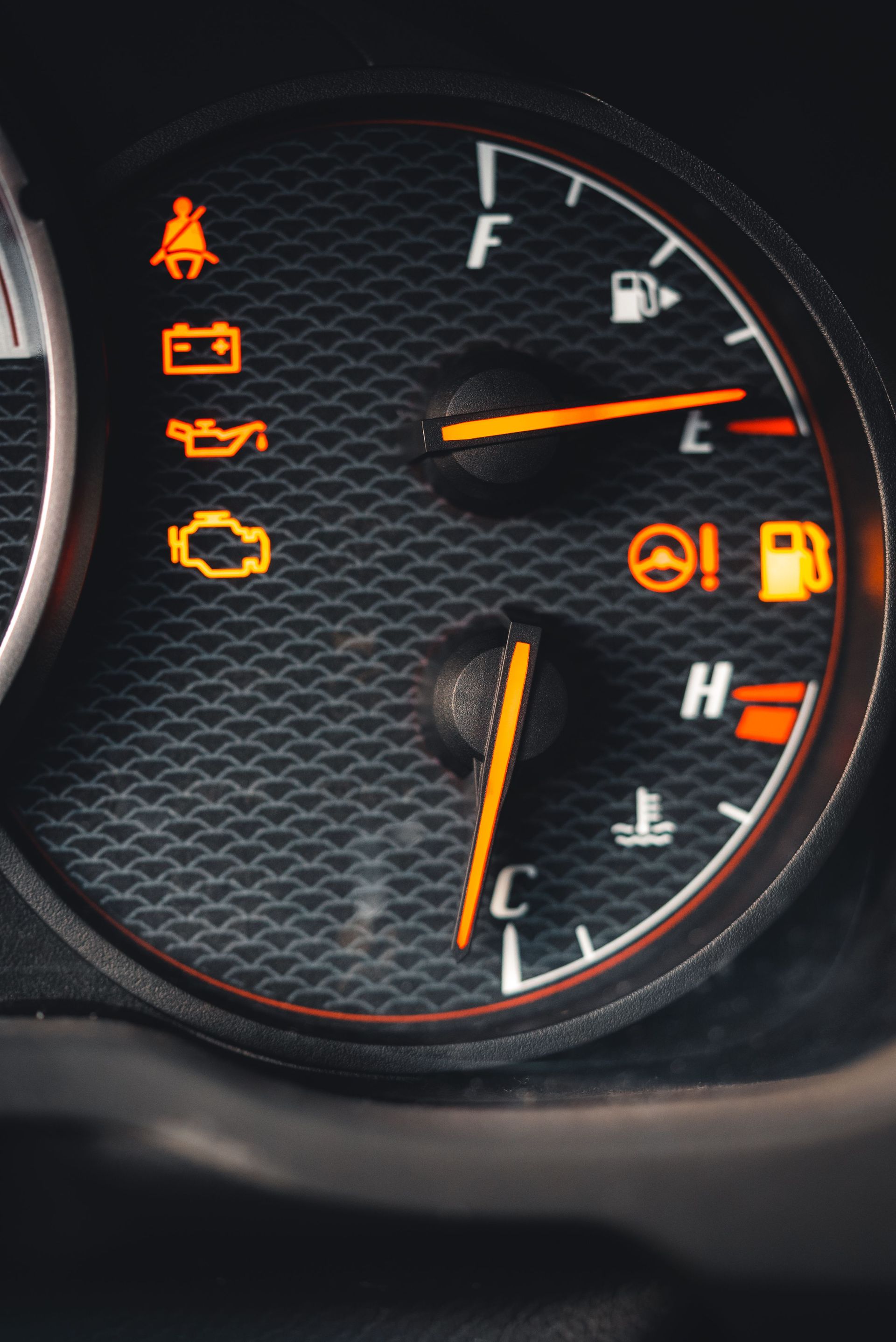 Car dashboard gauge cluster with warning lights illuminated and fuel and temperature needles visible