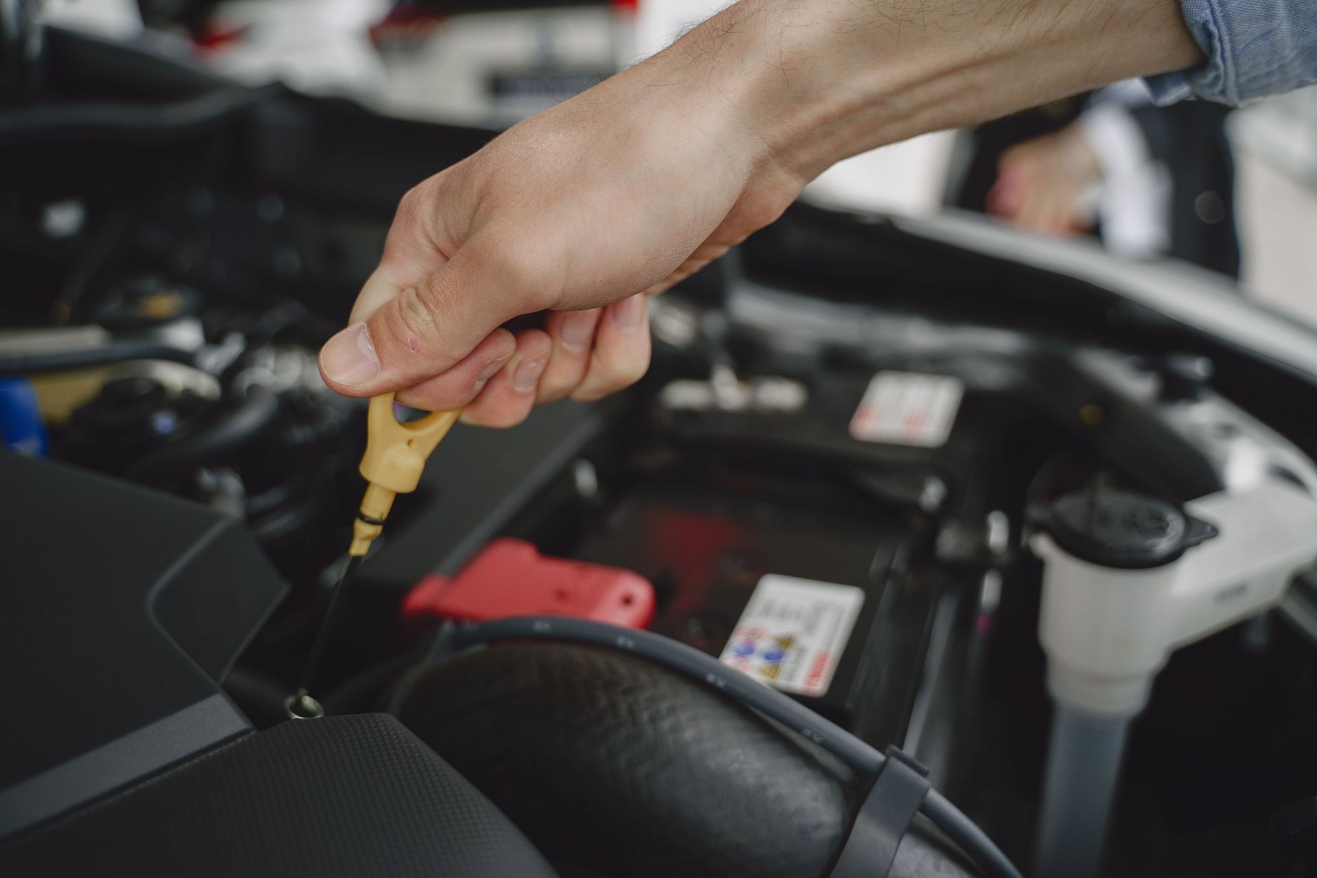 Hand checking engine oil with yellow dipstick in a car engine bay