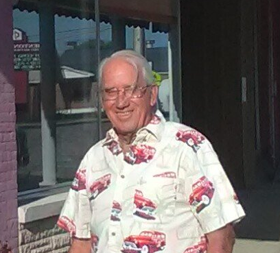 A man wearing a shirt with cars on it is standing in front of a building.