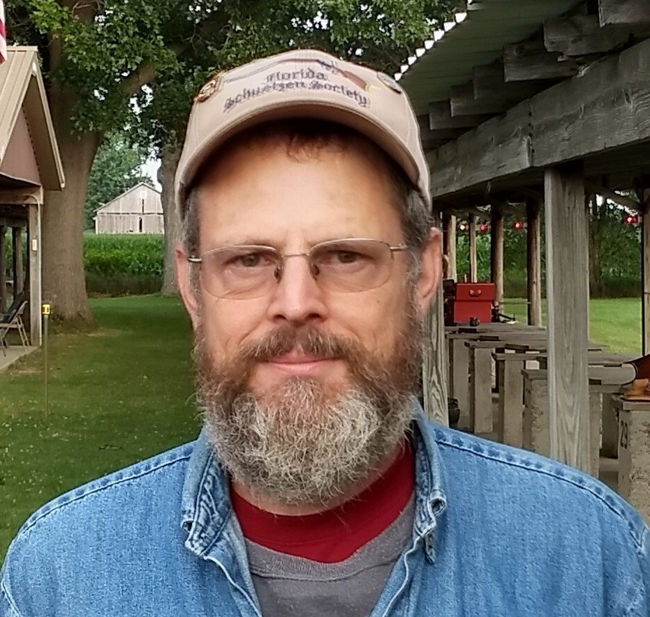 A man with a beard and glasses wearing a hat that says ' busch ' on it