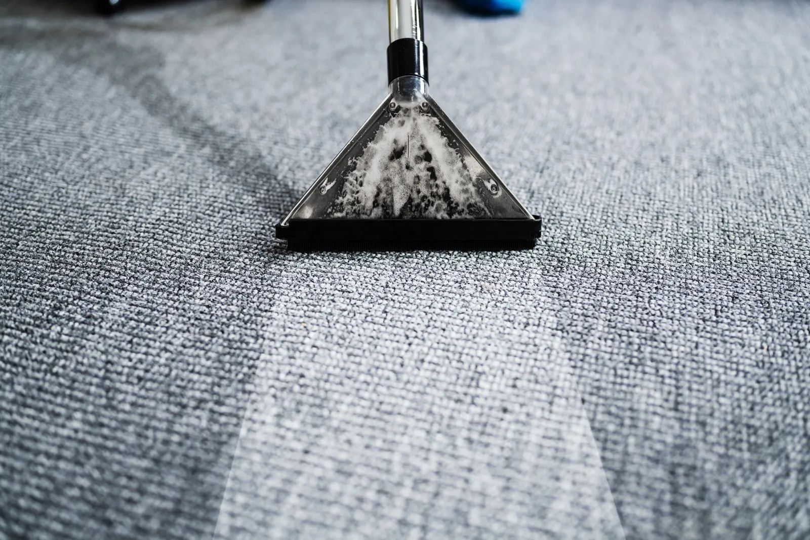 A carpet cleaning machine nozzle extracting dirt from a gray carpet, leaving a clean path.