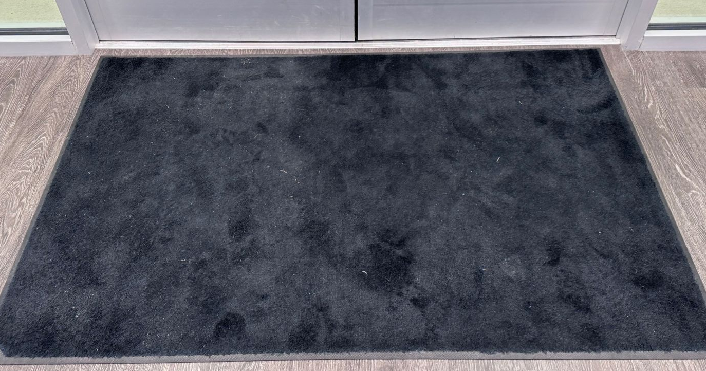 Black rectangular doormat in front of a white door on a wooden floor.