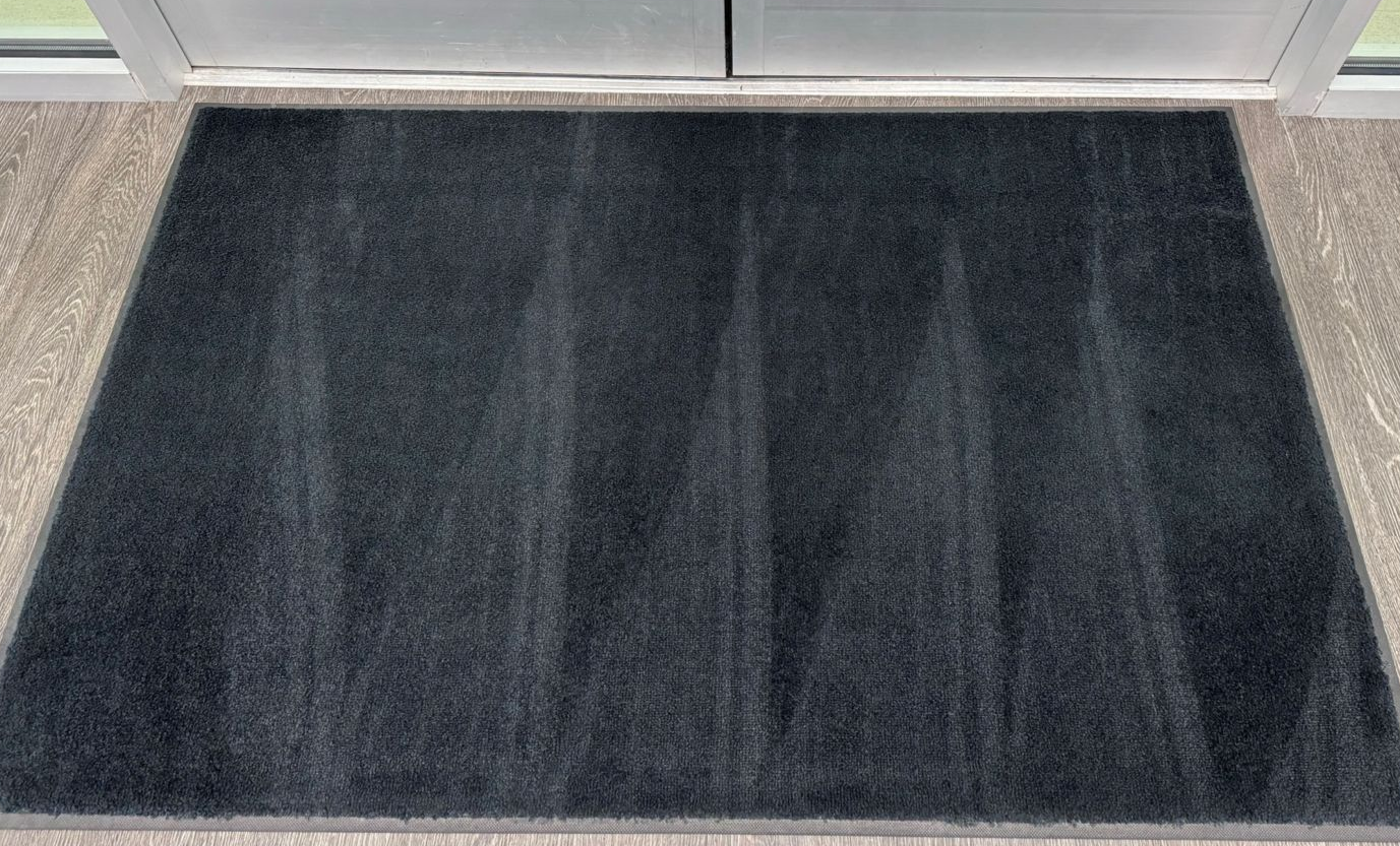 Black rectangular doormat in front of a door on a wood-grain floor.