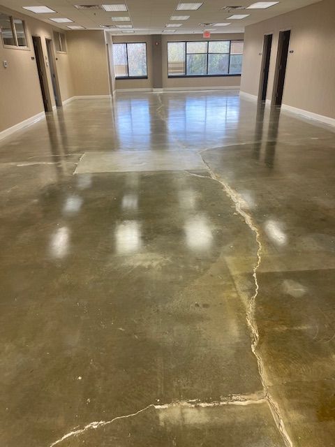 Polished concrete floor in a commercial space, with visible cracks and repaired sections.
