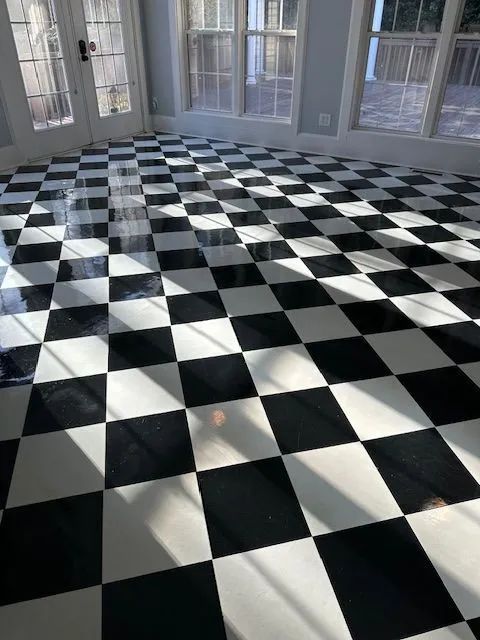 Black and white checkered floor in a sunlit room, with windows and a door in the background.