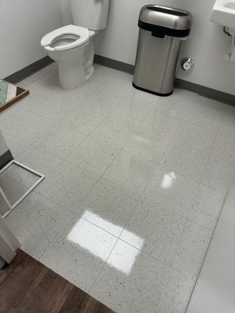 Bathroom with a toilet, trash can, and speckled floor tiles.