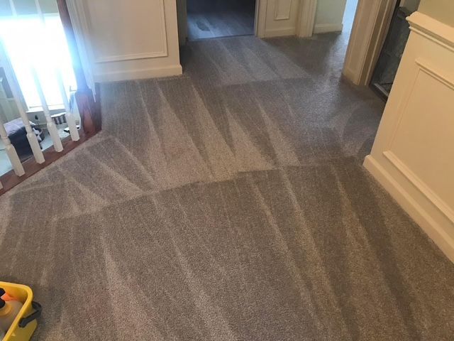 Gray carpet in a hallway with a striped pattern, leading to another room. White trim on the walls.