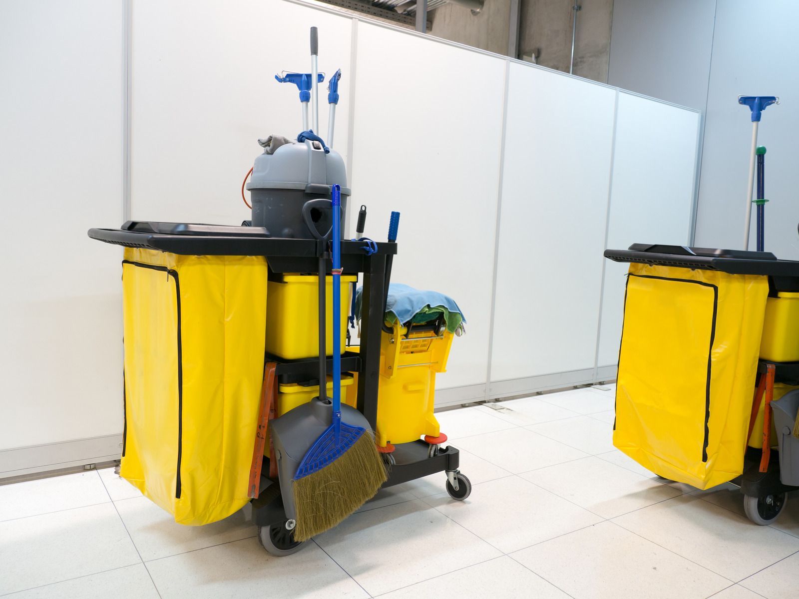 Two yellow cleaning carts on wheels, stocked with cleaning supplies, against a white wall.