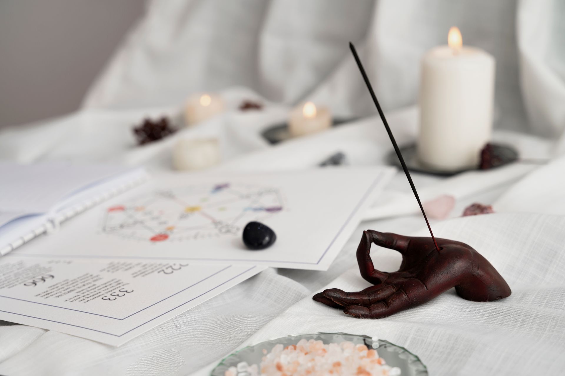 Porte-encens en forme de main avec de l'encens qui brûle. Bougies, cristaux et cartes ésotériques sur tissu blanc.