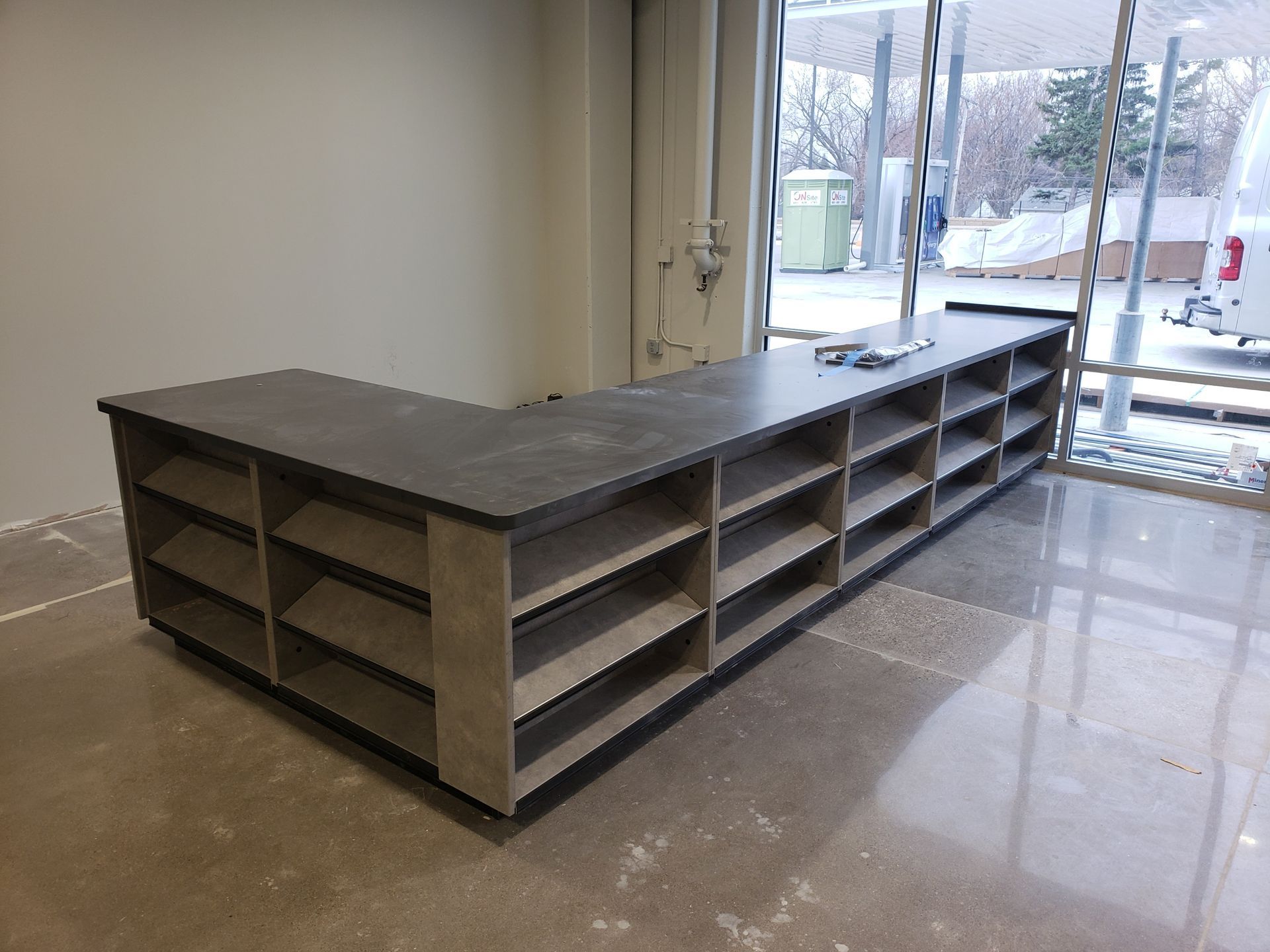 A long counter with shelves in a room with a window.