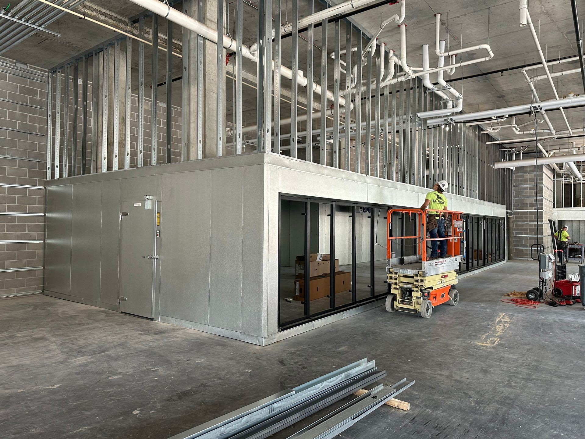 A man is standing on a scissor lift in a building under construction.