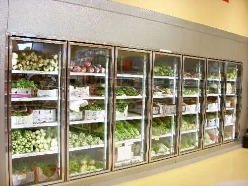 A row of refrigerators filled with vegetables in a grocery store