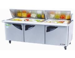 A stainless steel salad prep counter with vegetables in it.