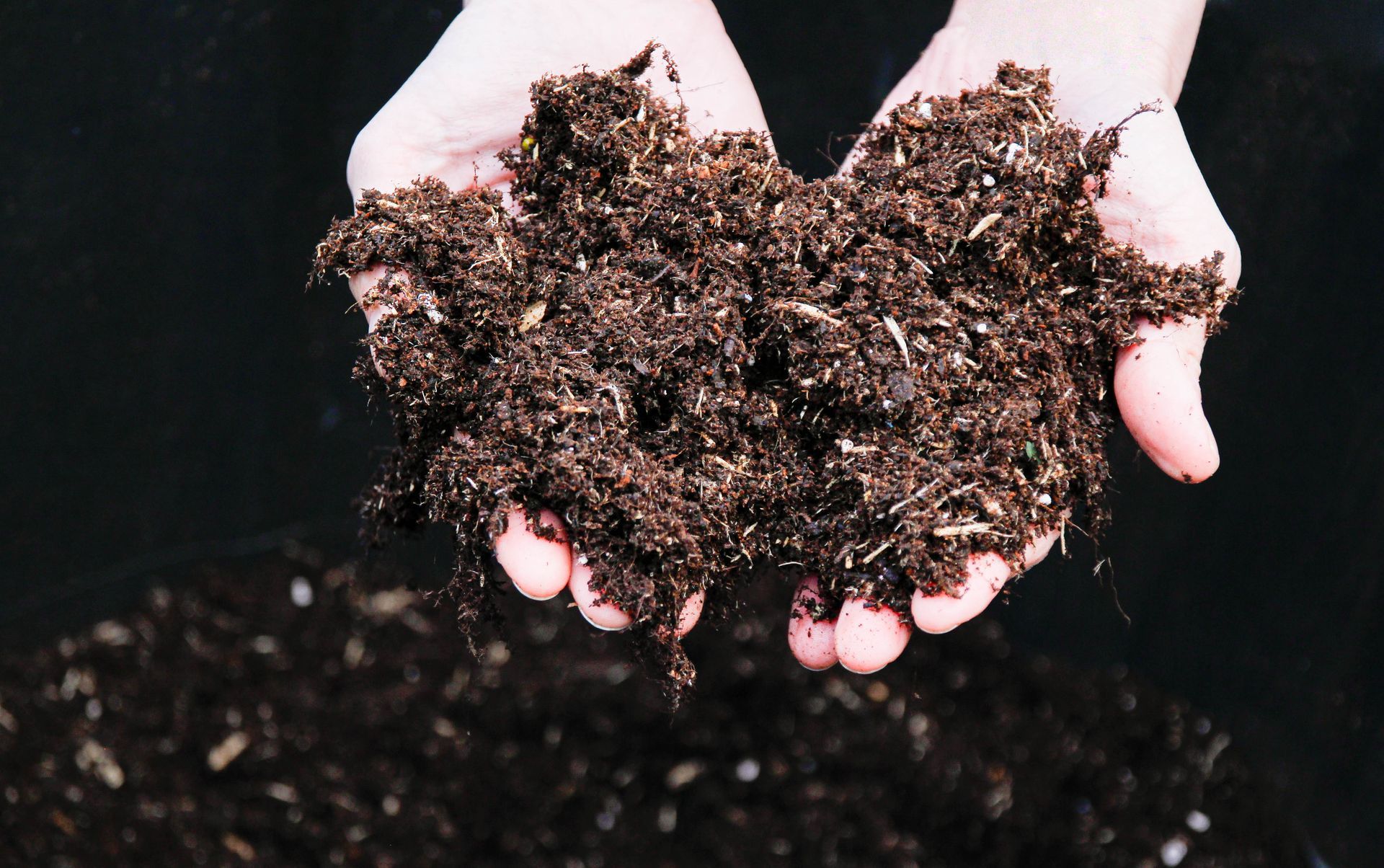 Mani che tengono in primo piano un pezzo di terra scura e ricca, compost.