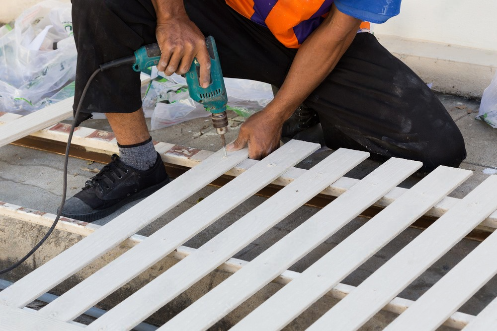 a man drills a hole in a piece of wood, building a fence for a house