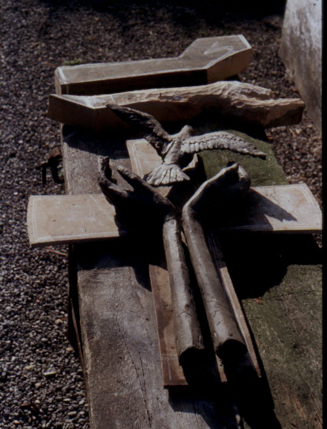 Wooden cross with outstretched arms, dove, and other carvings on a weathered surface, outdoors.