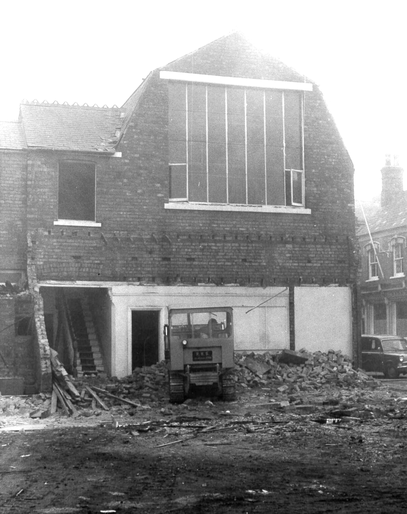 Demolition of brick building with large window, small tractor, debris pile, outdoors.